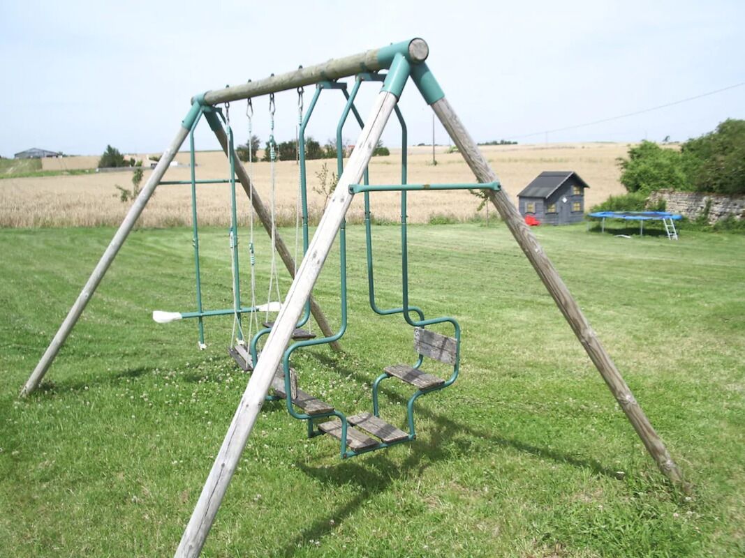 A swing set in a grassy field with a blue house in the background.