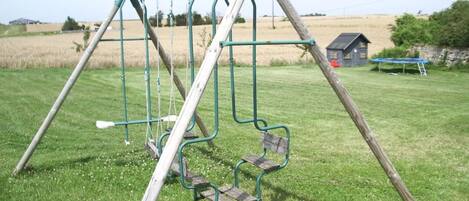 A swing set in a grassy field with a blue house in the background.