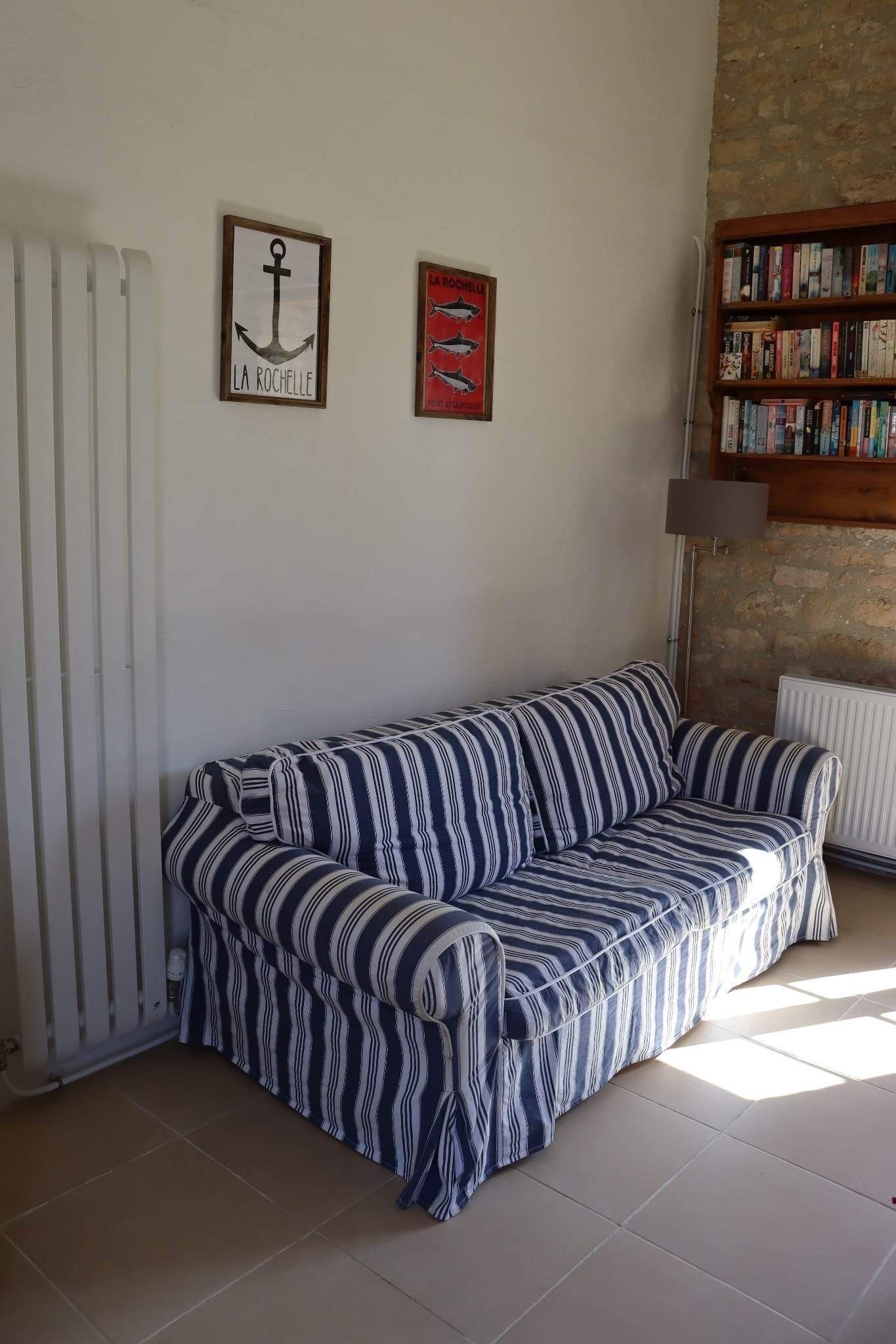 Un canapé à rayures dans un salon, avec un radiateur, une bibliothèque et deux tableaux encadrés accrochés au mur.