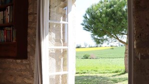 Une pièce rustique avec un mur en pierre, une bibliothèque en bois et une fenêtre donnant sur un champ verdoyant et un arbre.