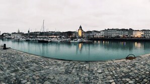 Une promenade en bord de mer avec un pavage en pierre, un port de plaisance avec des bateaux et des bâtiments historiques le long de la rivière.