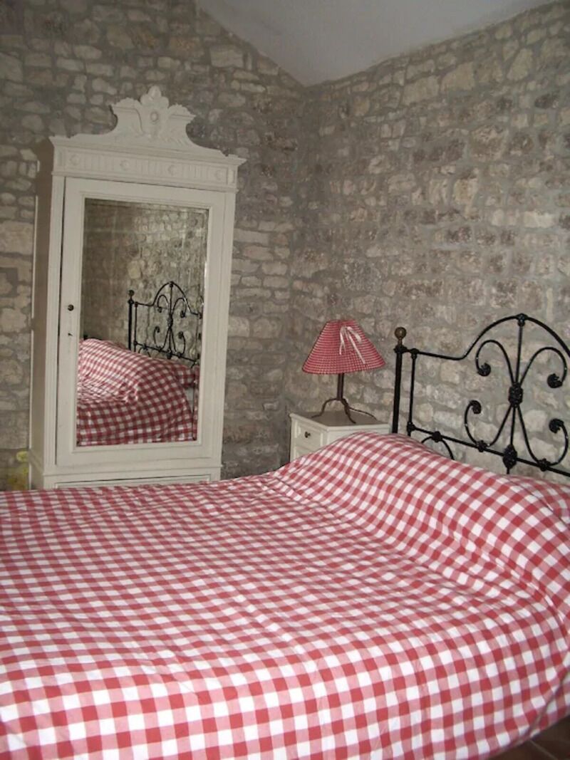 A bedroom with a checkered bedspread, a white dresser with a mirror, and a metal headboard.