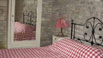 A bedroom with a checkered bedspread, a white dresser with a mirror, and a metal headboard.