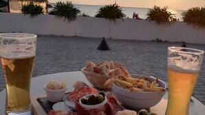 A table with a variety of food and drinks, including a tray of meats, olives, and bread, set against a backdrop of a sunset over the sea. - Pigeonnier - Traditional Farmhouse near La Rochelle. beaches 20 mins and a pool. (Landrais)