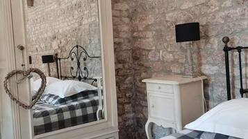 A bedroom with a stone wall, a large mirror, a bed with a checkered bedspread, a bedside table, and a nightstand.