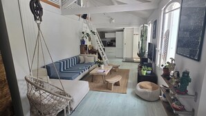 Un salon chaleureux avec un hamac, un canapé à rayures bleues, une table basse en bois et un petit pouf rond.