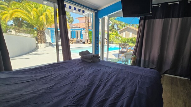 Une chambre d’hôtel avec un lit, une télévision et une vue sur une piscine et des bâtiments bleus.