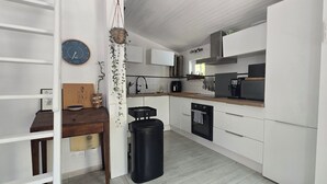 Une cuisine de taille réduite avec des meubles blancs, une poubelle noire, une horloge et une plante suspendue.