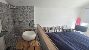 Une salle de bain avec une douche, un lavabo et un lit recouvert d’une couverture bleue.