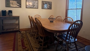 Un comedor con una mesa redonda, seis sillas, una araña y tres cuadros en la pared.