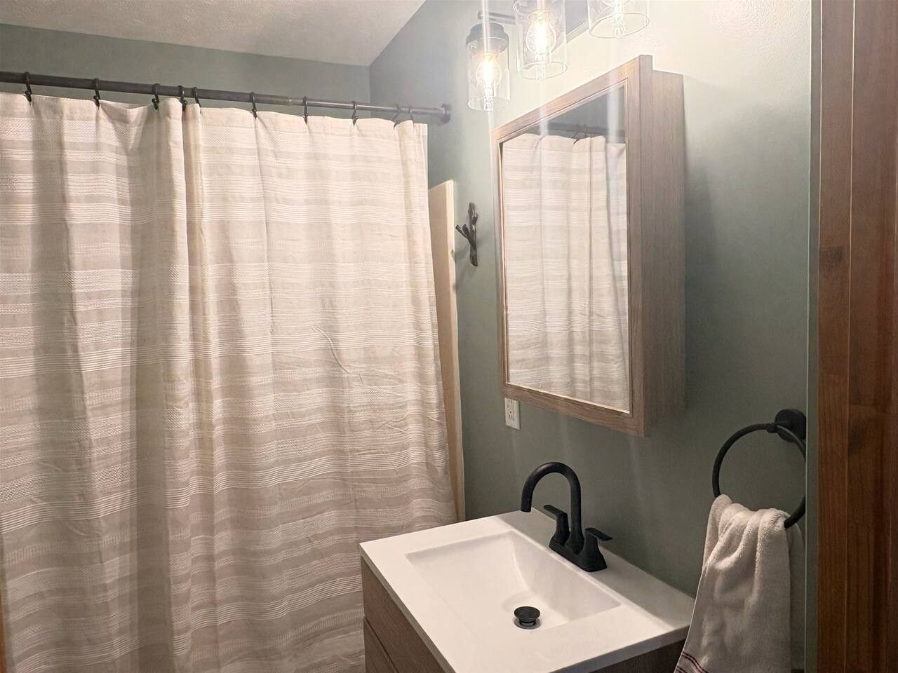 Une salle de bain avec un rideau de douche, un lavabo, un miroir et un porte-serviettes.