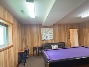 A room with a pool table, wooden walls, a ceiling fan, and a door.