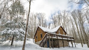 Una cabaña con fachada de madera, un porche y un paisaje cubierto de nieve.