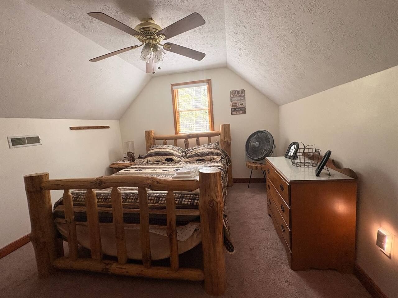 A bedroom with a wooden bed, a dresser, a ceiling fan, and a window.