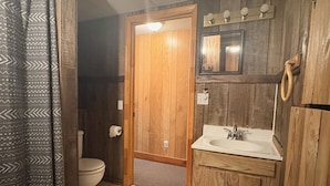 Un baño con puerta de madera, inodoro, lavabo y espejo.