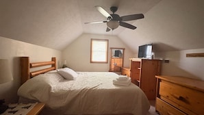 Un dormitorio con cama, cómoda de madera, mesita de noche y ventilador de techo.