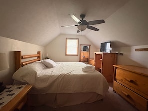 Una camera da letto con un letto, una cassettiera in legno, un comodino e una ventola a soffitto.