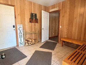 A cabin interior with a wooden wall, a welcome sign, a bench, and a door labeled 'Welcome to the Cabin.'