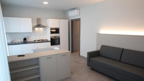 Eine moderne Küche mit weißen Schränken, einem eingebauten Ofen und einem Gasherd. Im Wohnbereich steht ein graues Sofa.