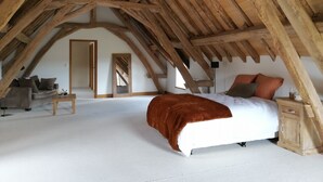Un dormitorio con techo de madera inclinado, una cama con manta marrón, una mesita de noche y un aparador.