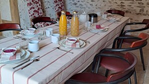 Una larga mesa de comedor dispuesta con platos, cubiertos y vasos, rodeada de sillas rojas en una sala rústica de paredes de piedra.