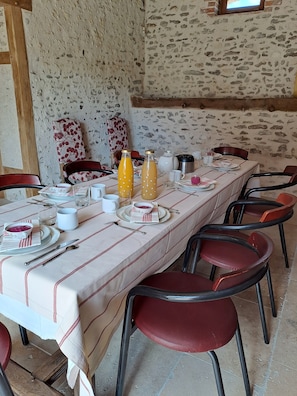 Une longue table à manger, dressée avec des assiettes, des couverts et des verres, entourée de chaises rouges dans une pièce rustique aux murs de pierre.