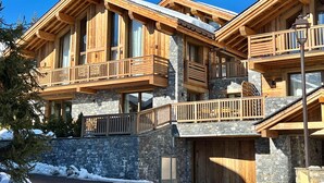 Un chalet en bois à plusieurs étages, doté de balcons, de murs en pierre et d’un garage.