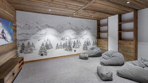 Une pièce dotée d’un plafond en bois, d’une fresque représentant un paysage de montagne enneigé et d’un coin salon avec des fauteuils en forme de poire.