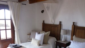 A room with two beds, a ceiling fan, a window with curtains, and a wooden ceiling. - Volcanic lava stone house short walk to the beach,  sea and mountain views (Arrieta, Lanzarote)