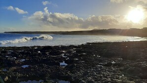 A rocky shoreline with waves crashing onto the rocks under a clear sky with the sun shining. - Volcanic lava stone house short walk to the beach,  sea and mountain views (Arrieta, Lanzarote)
