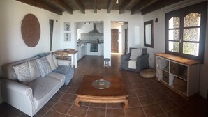A living room with a sofa, a coffee table, and a kitchen in the background. - Volcanic lava stone house short walk to the beach,  sea and mountain views (Arrieta, Lanzarote)
