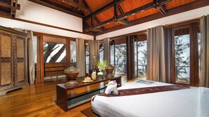 Une chambre spacieuse avec un grand lit, un plancher en bois et une vue sur les arbres par de grandes fenêtres.