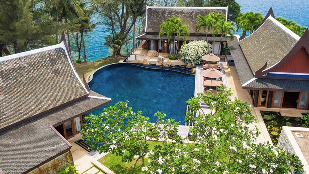 Un complexe hôtelier doté d’une piscine entourée d’une architecture traditionnelle, offrant une vue sur l’océan et un paysage verdoyant.