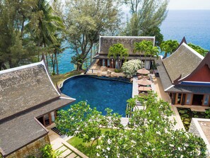 Un resort con piscina rodeada de arquitectura tradicional, vistas al océano y exuberante vegetación.