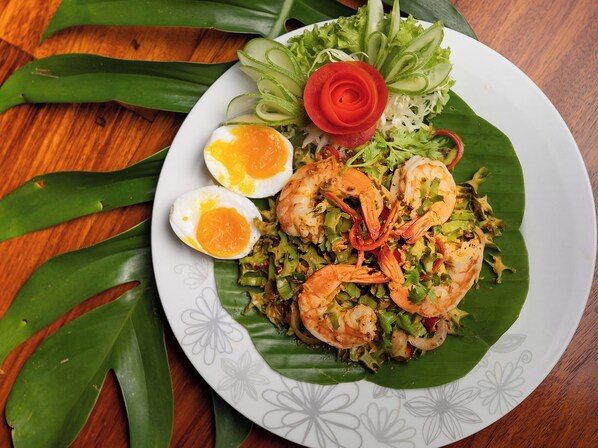 Un plato de comida con camarones, huevos cocidos y vegetales sobre una hoja de plátano.