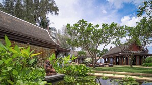 Un jardin paisible avec un étang, une végétation luxuriante et une architecture traditionnelle.