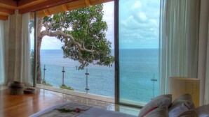 Un dormitorio con un gran ventanal con vista al mar, una cama con una rosa y suelo de madera.
