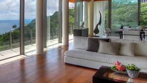 Un espacio habitable amplio con un sofá blanco, una mesa de centro con flores y vistas al mar a través de grandes ventanales.