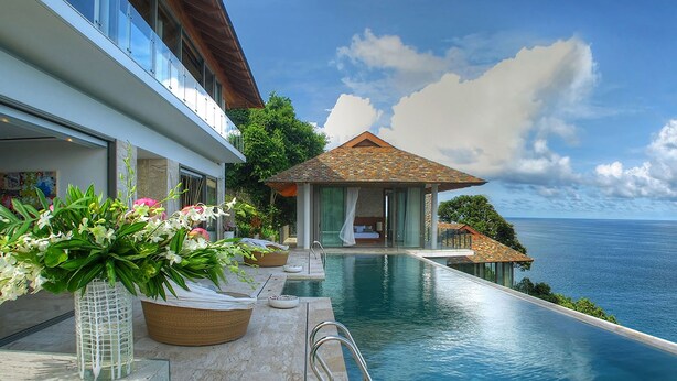 Una piscina infinita de lujo con vistas despejadas al océano, una cabaña privada y un jardín bien cuidado con flores.