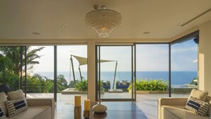A modern living room with a large glass door leading to a balcony with a view of the ocean. There are two sofas, a coffee table, and decorative candles. - Villa Samira by Elite Havens (Kamala)