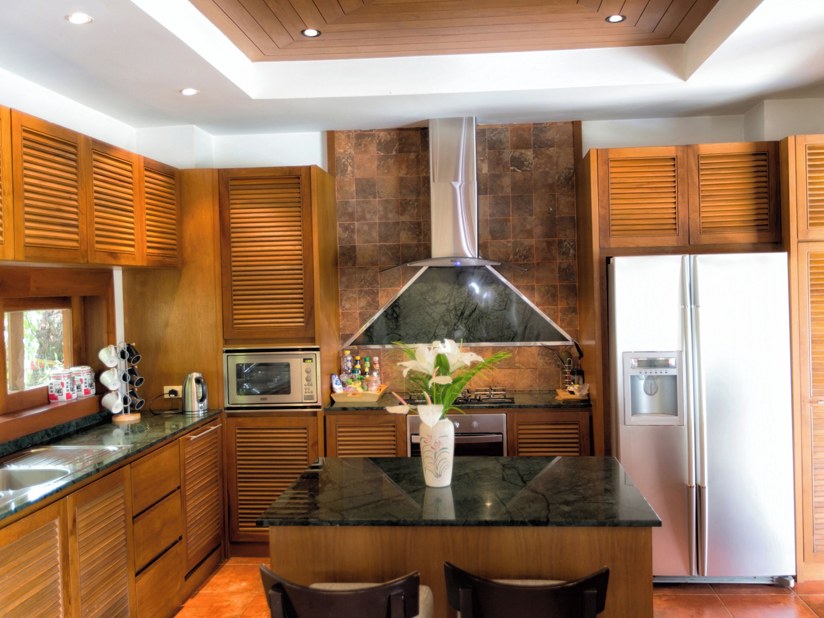A modern kitchen with wooden cabinets, a central island, stainless steel appliances, and a decorative vase with flowers.