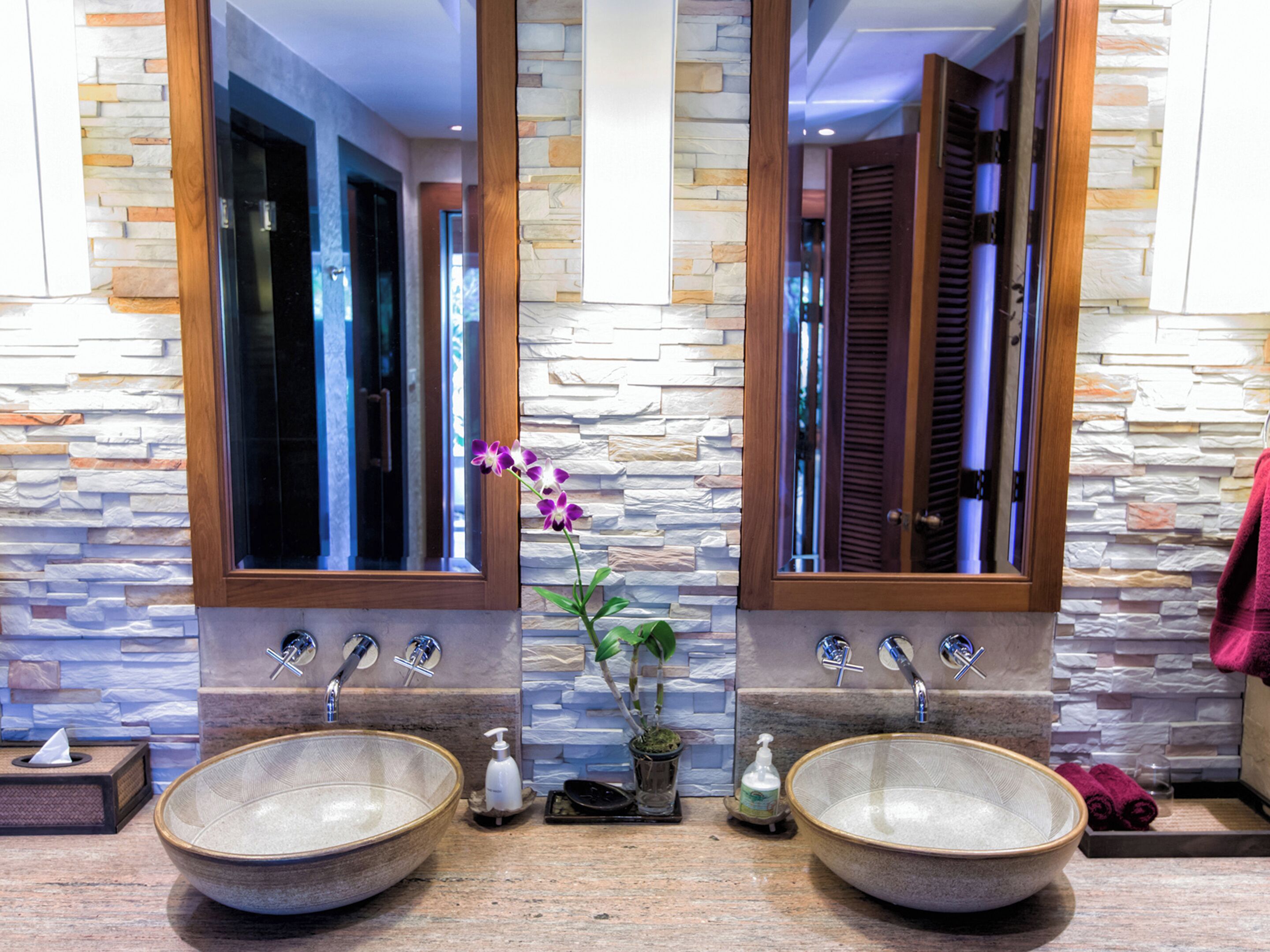 A bathroom with two large ceramic sinks, a mirror, and a stone wall.