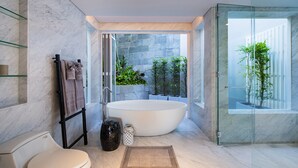 Un baño moderno con una bañera independiente, una cabina de ducha de vidrio y vistas a un jardín ajardinado.
