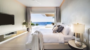 Habitación de hotel moderna con una cama grande, televisión, ventilador de techo y vista al océano.