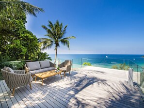 A deck with a sofa, chairs, and a coffee table overlooking a clear blue sea. - Villa Borimas by Elite Havens (Choeng Thale)