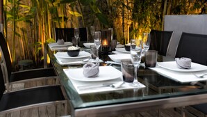 A dining table set for two with a glass top, surrounded by chairs, in a room with a tropical plant backdrop. - Villa Napalai (Choeng Thale)
