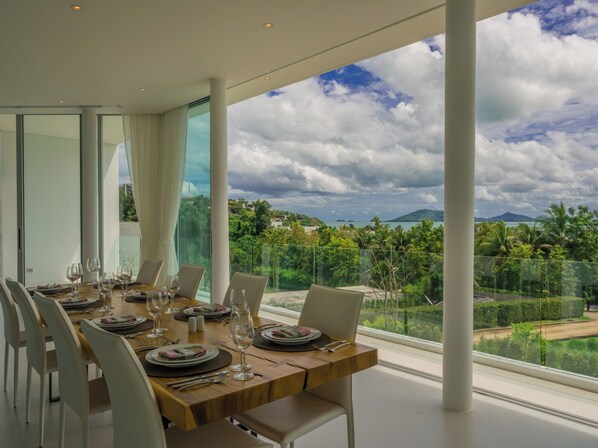 Ein Essbereich mit einem Tisch für sechs Personen, große Fenster mit Blick auf eine üppige Landschaft und ferne Berge.