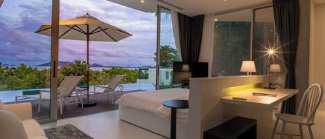 Habitación de hotel moderna con un ventanal grande, una cama, un escritorio y una zona de estar con vistas al mar.