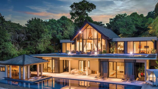 Una casa moderna de dos pisos con un balcón grande, piscina y un exuberante bosque de fondo.