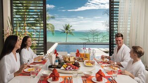 Mesa de comedor lista para una comida con vista al océano y palmeras.